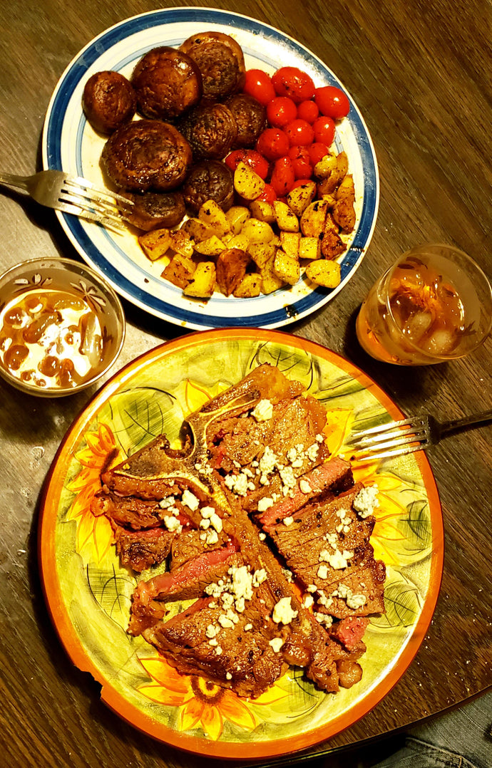 Dinner for two. A $12 porterhouse, medium rare with blue cheese, sauteed yellow potatoes, cherry tomatoes, and mushrooms, and two heavy hearth rolls with butter (not pictured). And two whiskeys.